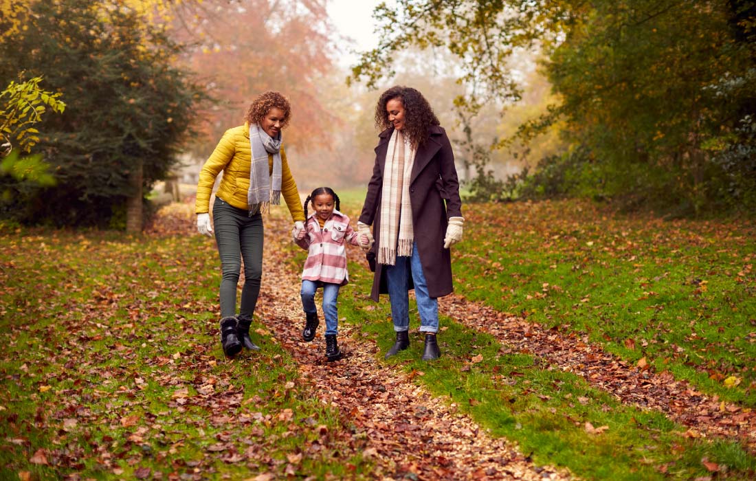 Black lesbian female couple holding hands with dauthger on walk through autumn countryside together